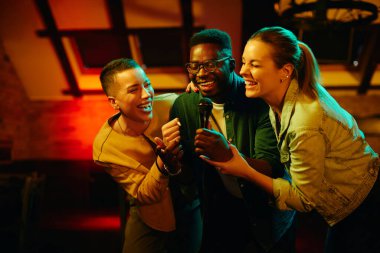Happy African American man and his female friends singing karaoke during their night out in a bar.