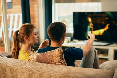 Young woman eating popcorn and watching movie on TV with her boyfriend at home. 