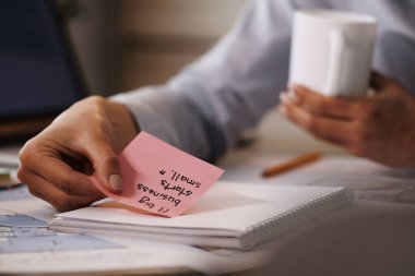 Close-up of businesswoman putting inspirational adhesive note on her notebook while working in the office.