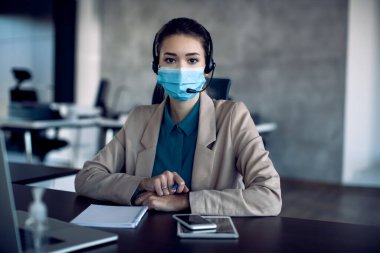 Businesswoman with face mask having conference call in the office and looking at camera. 