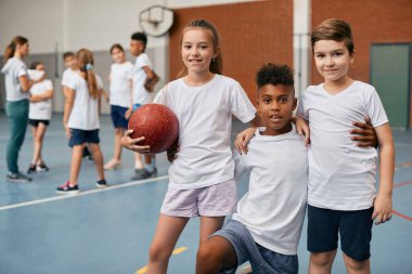 African American boy and his schoolmates embracing and looking at camera during physical activity class.