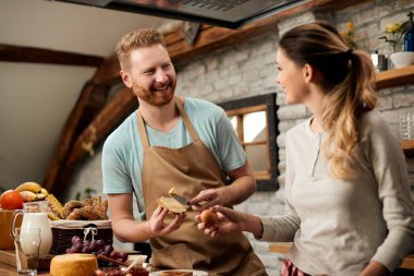Happy redhead talking to his girlfriend while making breakfast together in the kitchen. 