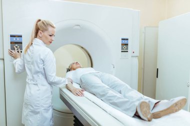 Female doctor starting CT scan procedure of senior patient at medical clinic. 