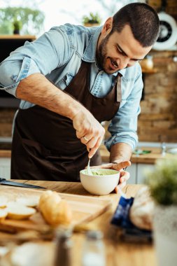 Young smiling man enjoying while making healthy food in the kitchen, 