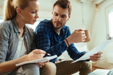 Genç bir adam, karısıyla oturma odasında finans durumunu gözden geçirirken kahve içiyor.. 