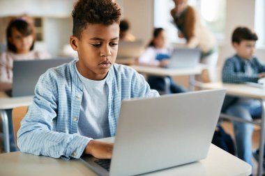 Black schoolboy using laptop during computer class at school.