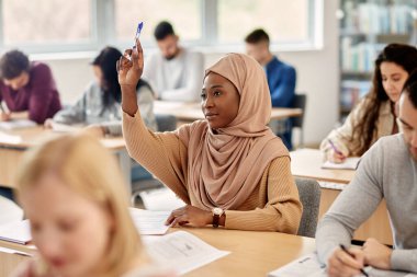 Female Islamic student raising her arm to ask a question during lecture in the classroom.