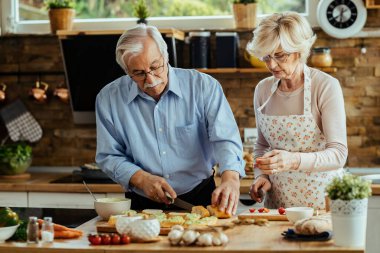 Mature husband and wife preparing bruschetta in their kitchen. 