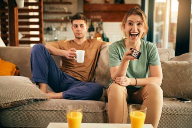 Happy woman having fun while changing channels and watching Tv with her boyfriend at home. 