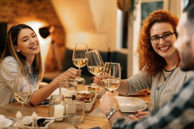Small group of happy people toasting while having dinner in dining room. Focus is on redhead woman.