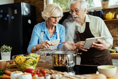 Mature couple using digital tablet while preparing food in the kitchen. 