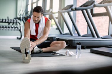 Athletic man warming up for sports training and stretching on the floor in health club. 