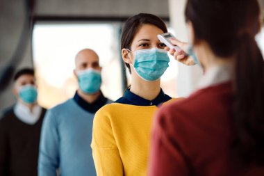 Businesswoman with face mask on a temperature checkpoint before and educational event in board room.