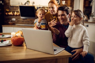 Happy family sending kisses while making video call over laptop on Thanksgiving at home. 
