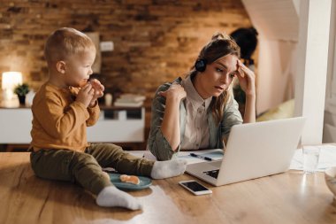 Distraught mother working on a computer while being with her son at home.