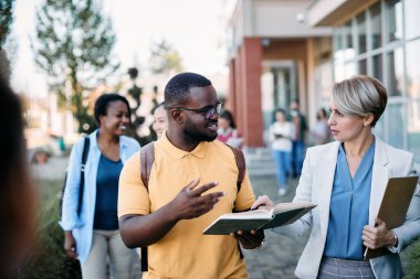 Female university teacher communicating with African American student at campus.