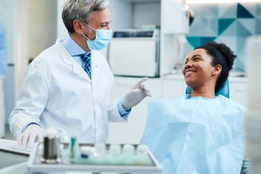 Happy dentist talking to black female patient during dental exam at dentist's office.