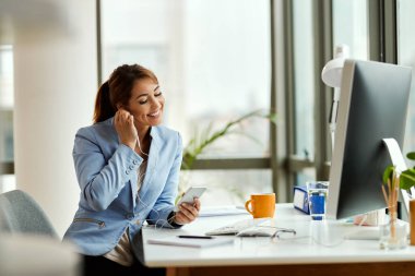 Young businesswoman relaxing while using mobile phone and listening music over earphones in the office.