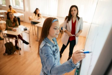 Female student writing on interactive whiteboard during a class at high school. 