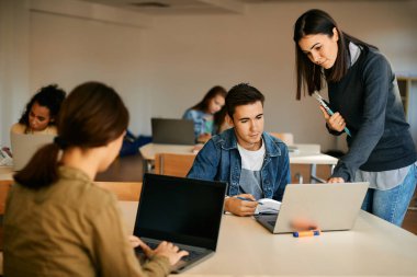 Computer science teacher assisting her student with e-learning during a class at high school.