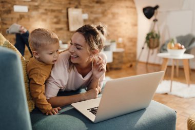 Happy mother and son relaxing on the sofa and using computer in the living room.