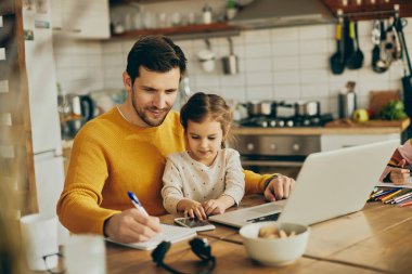 Smiling father working at home while daughter is sitting on his lap.