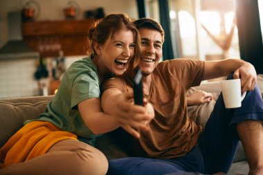 Young couple having fun while watching TV and struggling about remote controller at home.