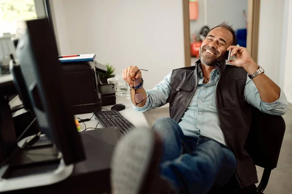 Happy auto mechanic relaxing in the office and talking on mobile phone.