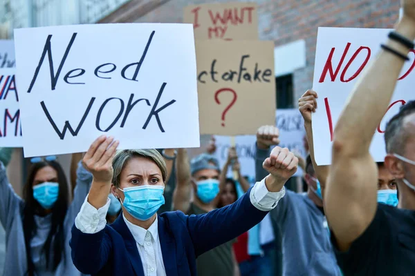 Crowd unemployed people participating in public demonstrations due to coronavirus epidemic. Focus is on businesswoman carrying banner with \'need work\' inscription.