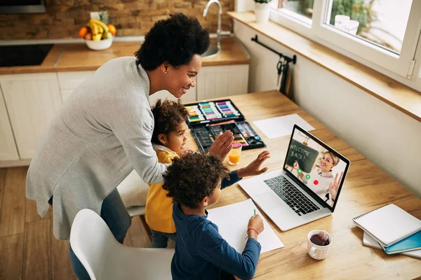 Happy black mother and kids waving to a teacher while having video call over a computer from home.