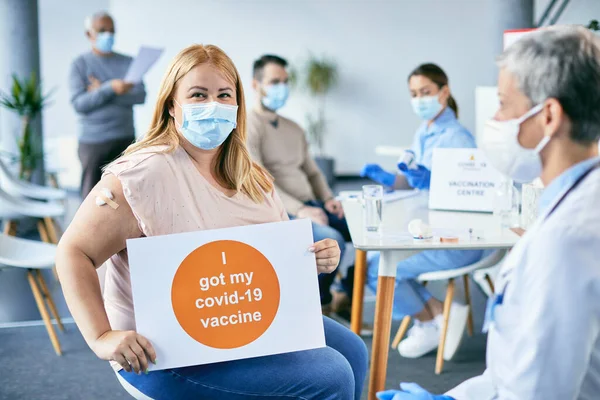 Happy woman with face mask getting vaccinated against coronavirus and holding supportive placard with \