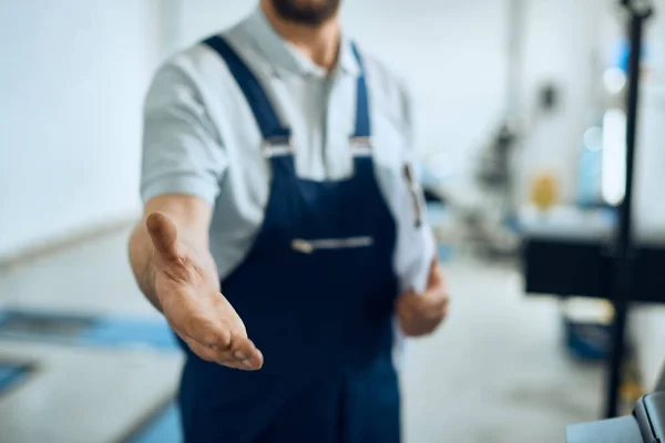 Close-up of car mechanic greeting someone and offering handshake while working at auto repair shop.