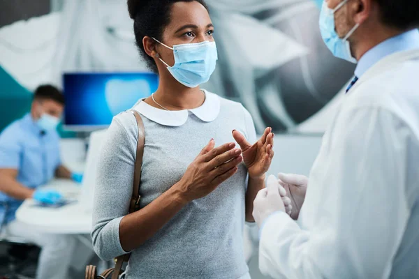 Black woman and her dentist wearing face masks while communicating at dentist\'s office.