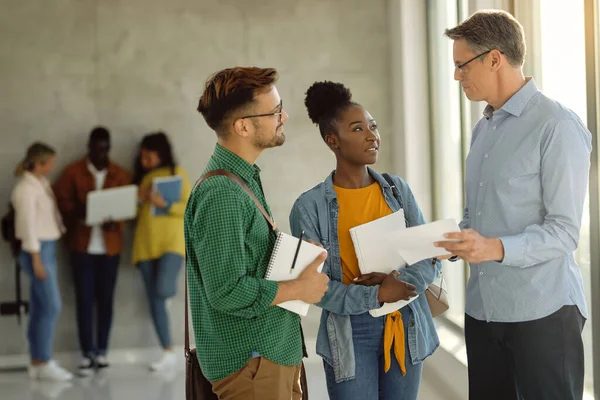 University teacher and his students communicating in a hallway. Focus is on female  African American student. 