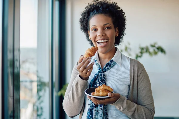 Young Black Businesswoman Eating Croissant Office Looking Camera —  Fotos de Stock