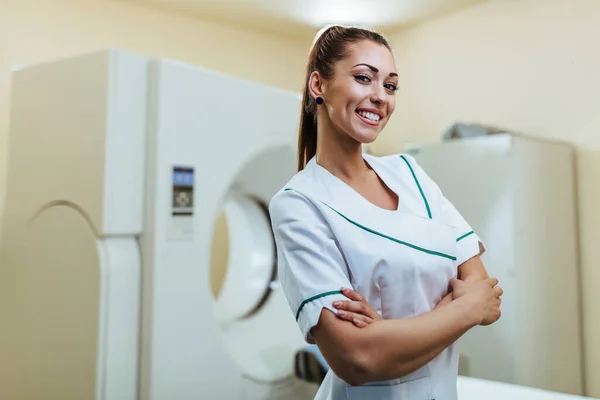 Portrait of confident female radiologist in front of CAT scan machine at medical clinic.