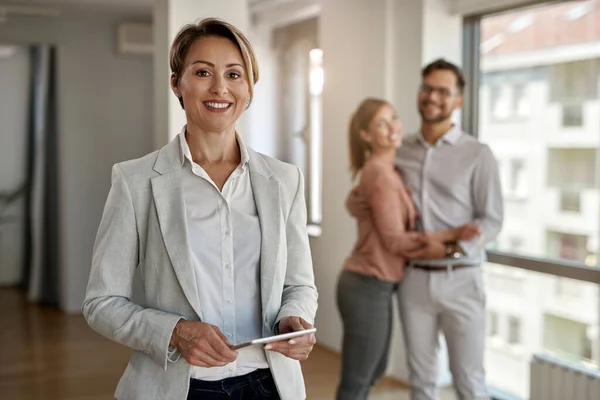 Portrait of female real estate agent looking at the camera while happy couple in standing in the background.