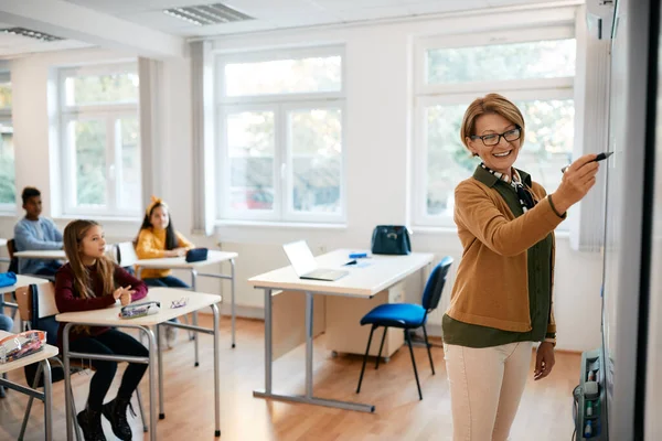 Happy Elementary Teacher Giving Lecture Her Students While Writing Whiteboard — Stok Foto