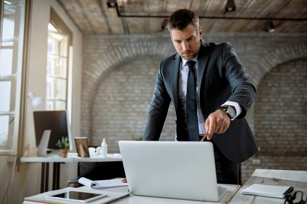 Mid adult businessman pointing at laptop screen while reading an e-mail in the office. 