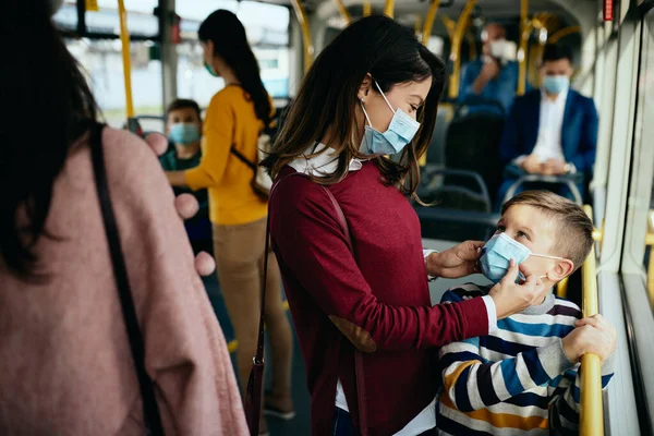 Smiling mother ad her son wearing protective face masks in a public bus due to coronavirus pandemic.
