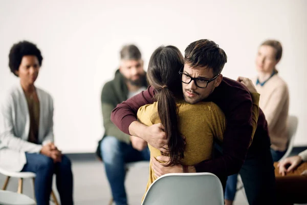 Young sad man hugging female participant of group therapy during the meeting.