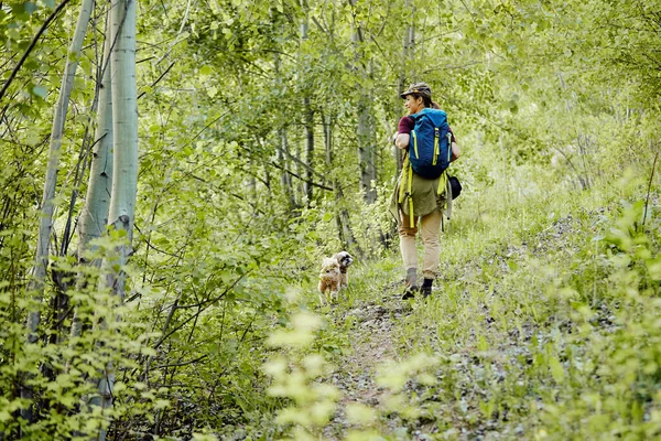 Happy woman carrying backpack while hiking and walking with her dog through nature.