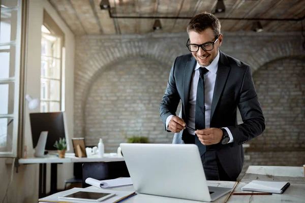 Happy entrepreneur reading something on a computer while standing at his office desk.