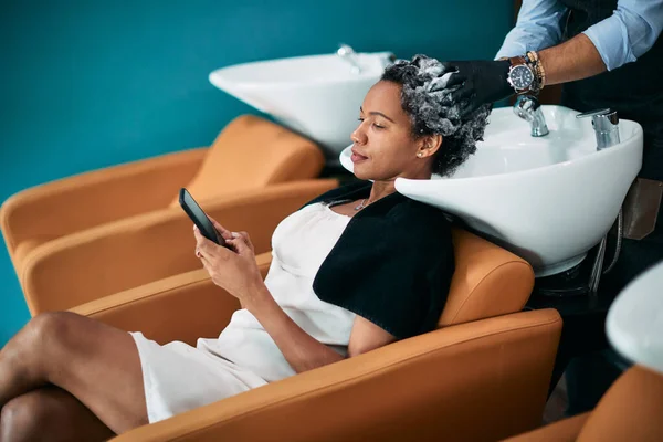 African American Woman Using Smart Phone While Getting Her Hair — Zdjęcie stockowe