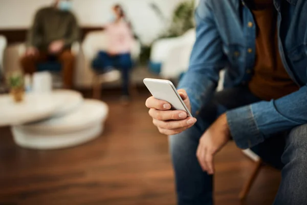 Close-up of man text messaging on mobile phone while waiting for medical appointment at doctor's office.