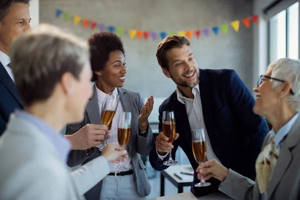 Group of happy business colleagues drinking Champagne and communicating while celebrating on a party in the office.