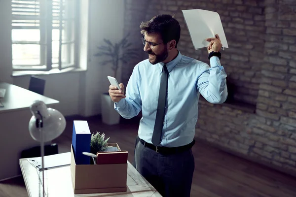 Angry businessman reading text message on mobile phone after being fired at work.