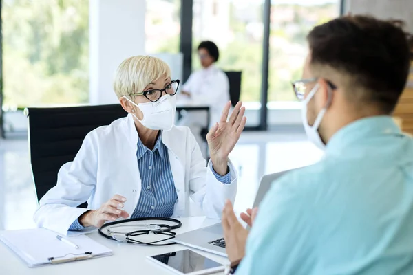 Ώριμη Γιατρός Φορώντας Προστατευτική Μάσκα Προσώπου Ενώ Επικοινωνεί Τον Ασθενή — Φωτογραφία Αρχείου