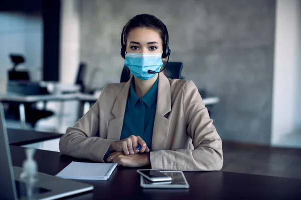Businesswoman with face mask having conference call in the office and looking at camera.