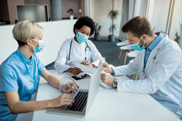 Medical experts wearing face masks and cooperating while going through reports at the hospital. Focus is on black female doctor.